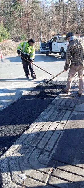 2 men spreading asphalt near a sidewalk.