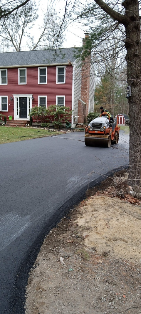 Asphalt roller compacting newly installed residential driveway near home