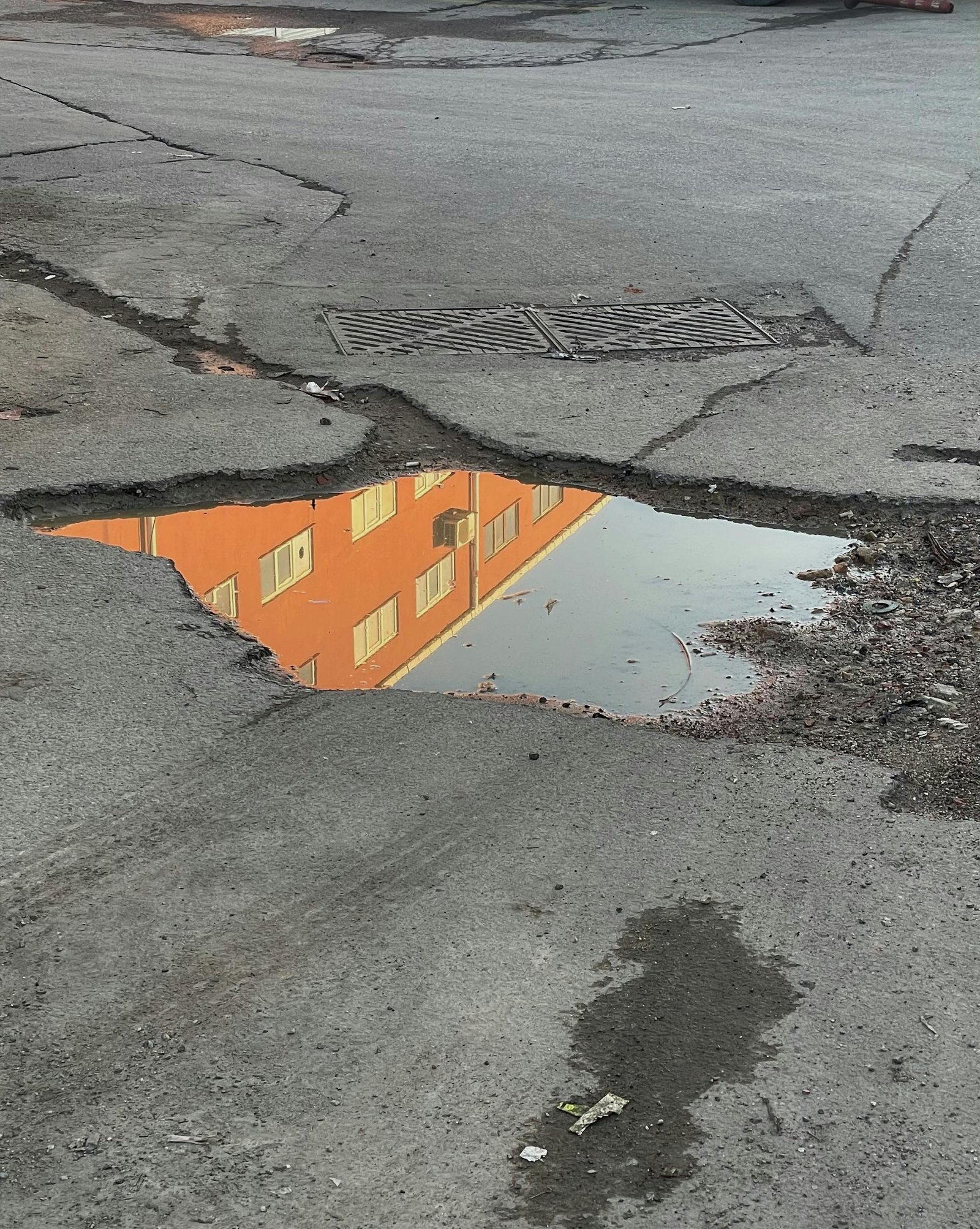 Urban street puddle reflecting orange building. Grungy city street scene with cracks and textures.